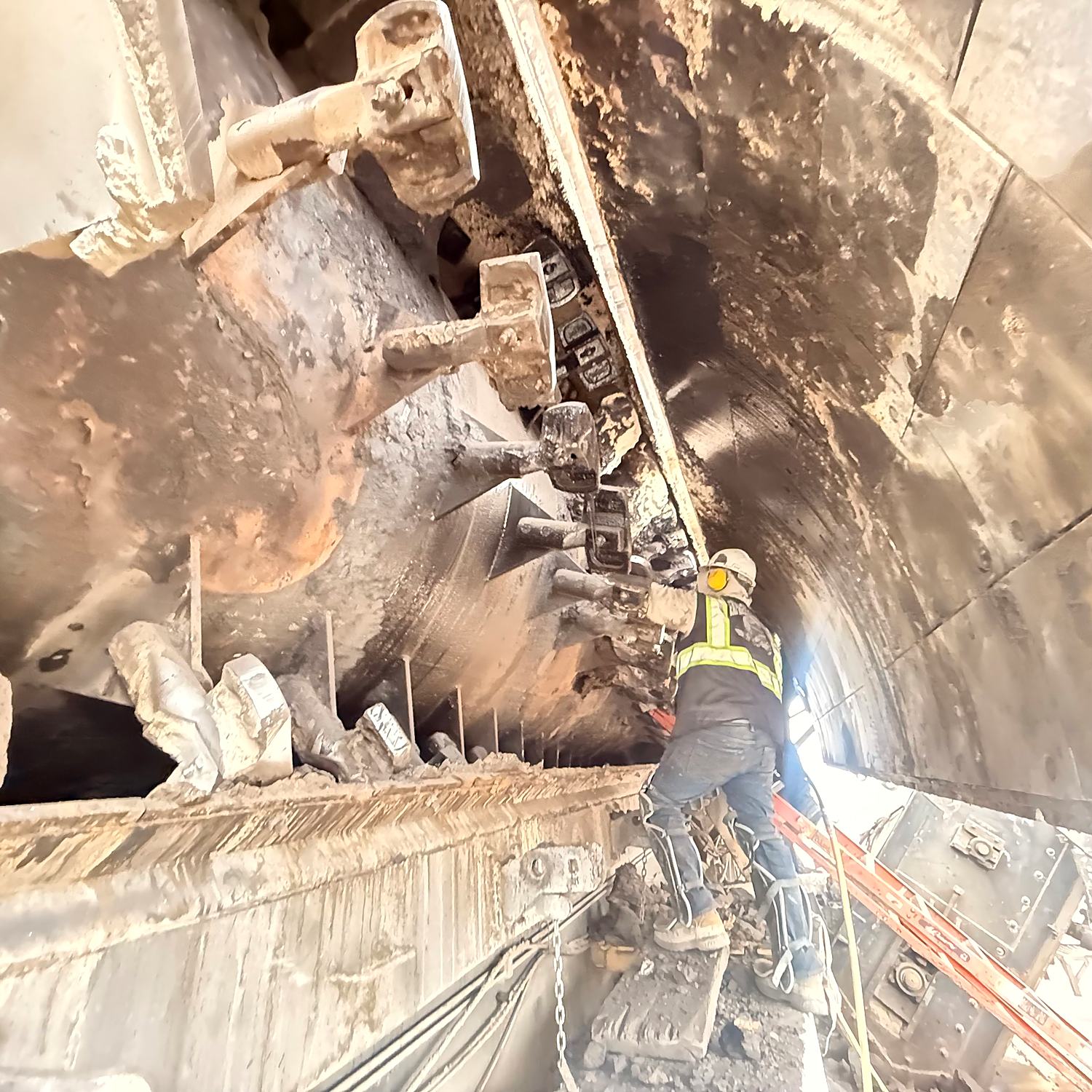 Technician in hard hat and high visibility vest removing hardened asphalt buildup from the flights inside an asphalt plant drum
